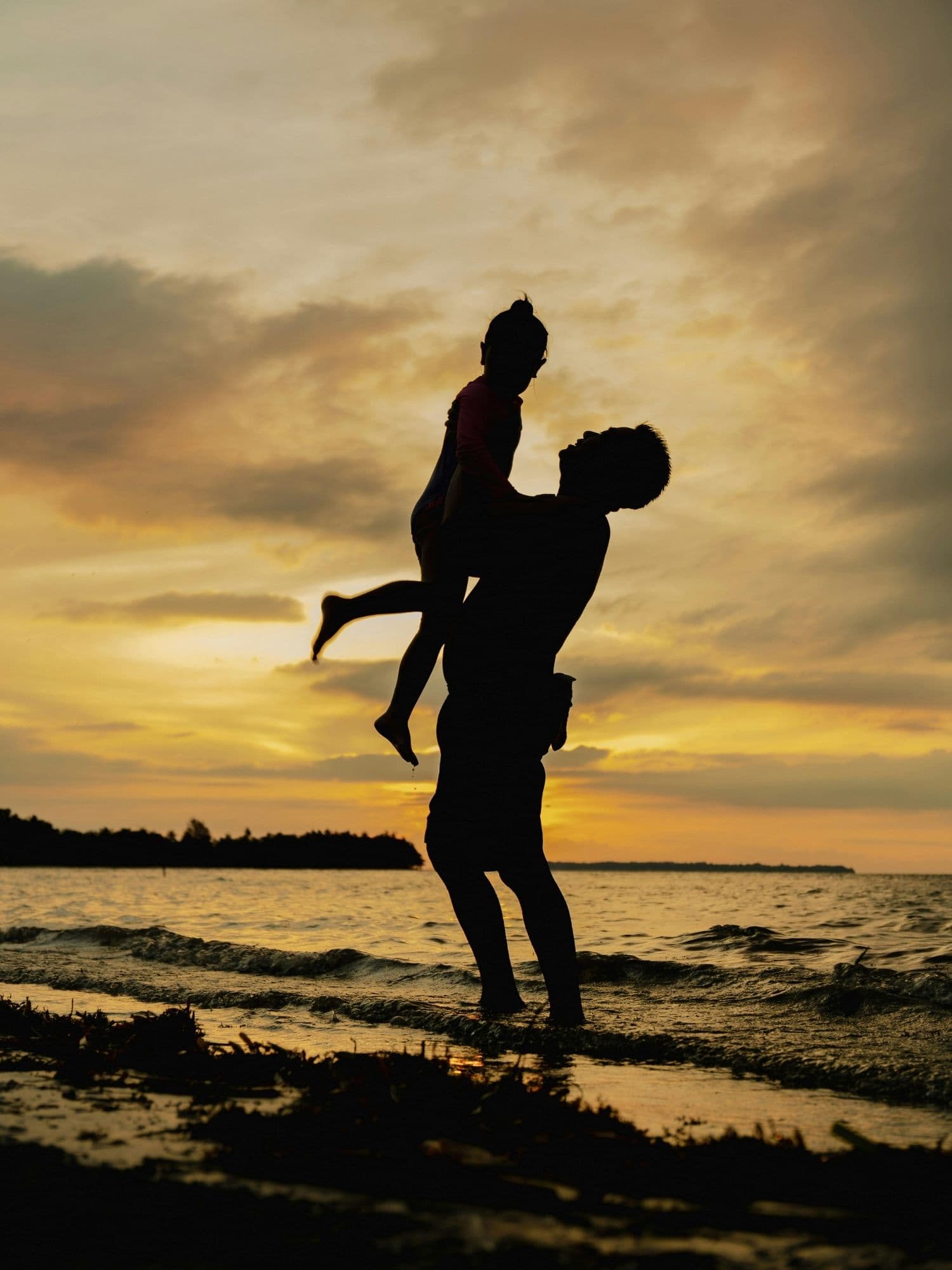 Dad lifting daughter at beach sunset